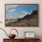 Walnut floater framed canvas featuring a sandy beach with figures relaxing near water's edge, displayed above a cabinet in a soft-toned living room.