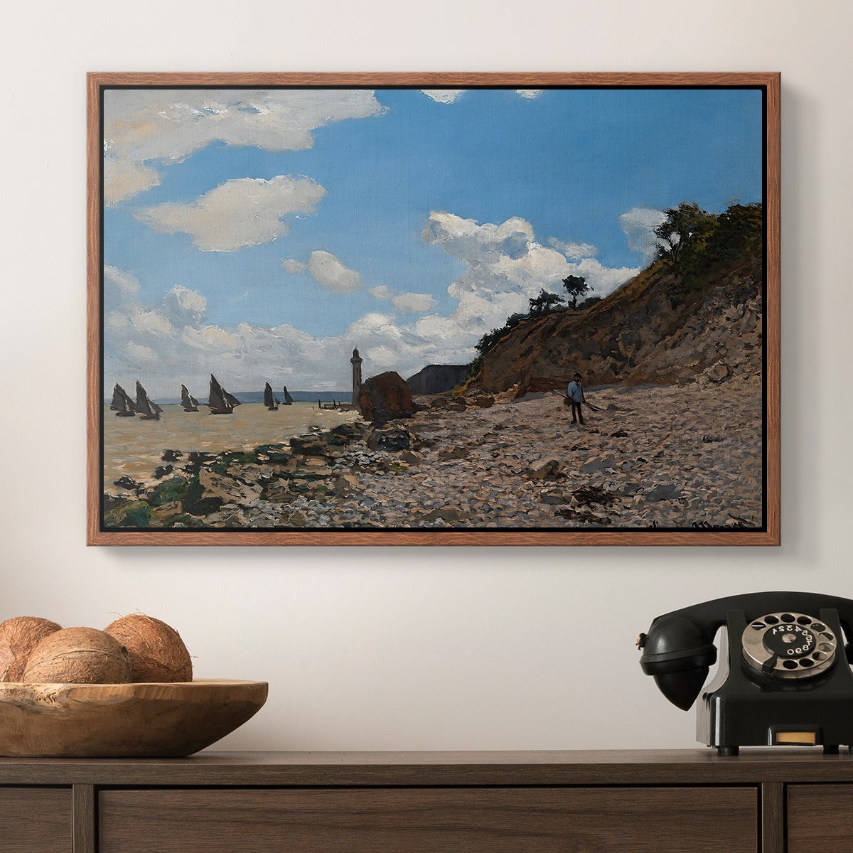 The Beach at Honfleur, 1864 by Claude Monet in a walnut floater framed canvas displayed above a console table in a hallway, featuring a coastal landscape with boats and people along shore.