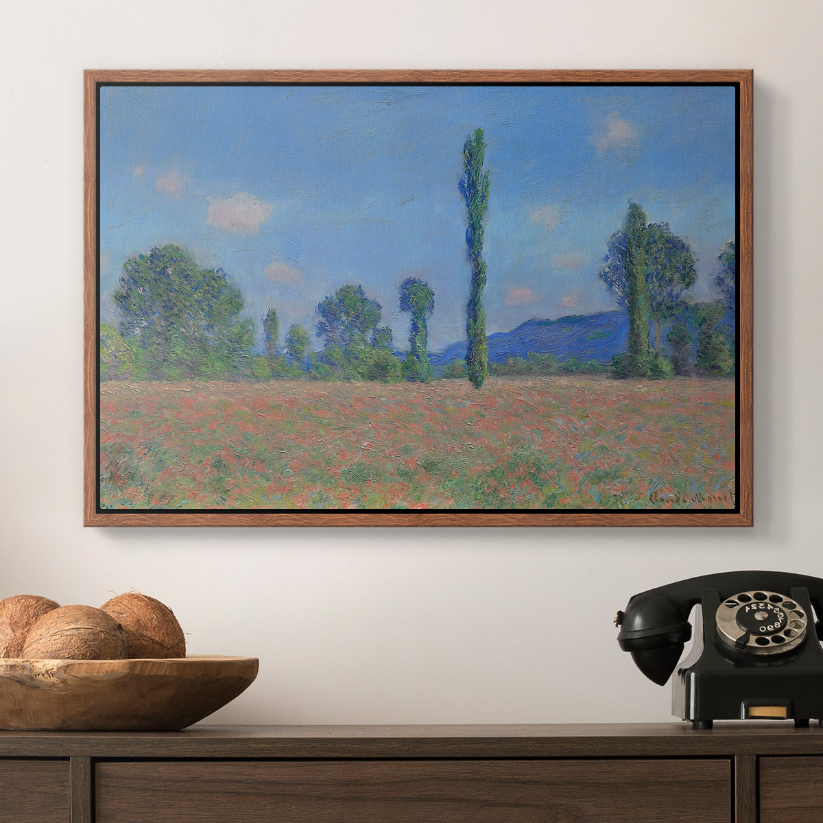 Poppy Field (Giverny), 1890-1891 by Claude Monet in a walnut floater framed canvas displayed above a console table in a hallway, featuring a rural field filled with red blossoms beneath open sky.