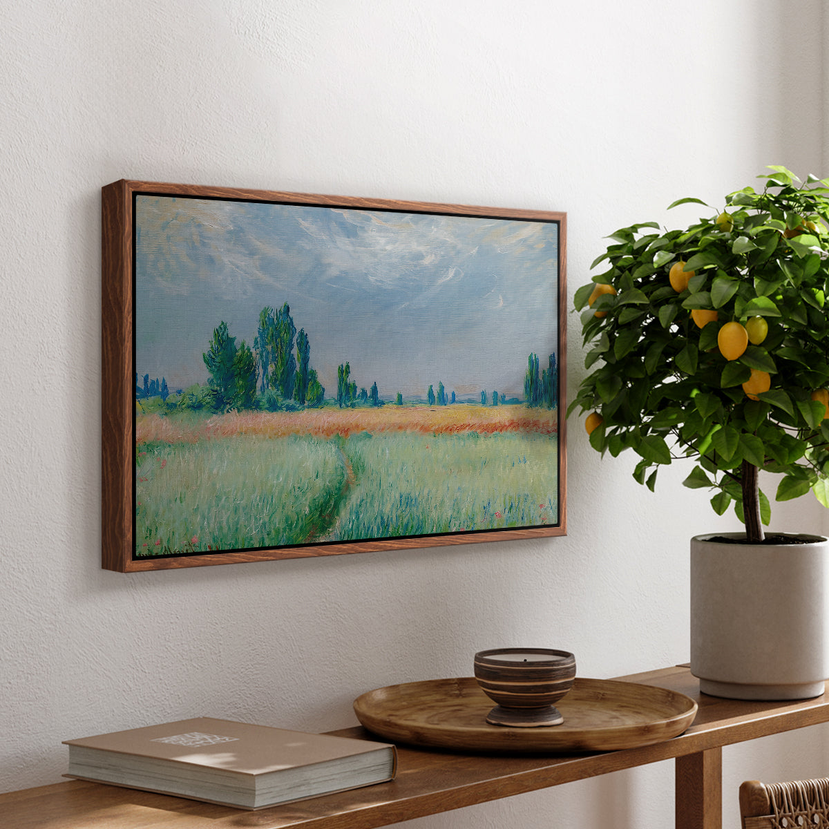 The Wheat Field (Champ de Blé), 1881 by Claude Monet, presented in a walnut floater framed canvas featuring a golden wheat field stretching across landscape under soft sky, displayed above a hallway console table.