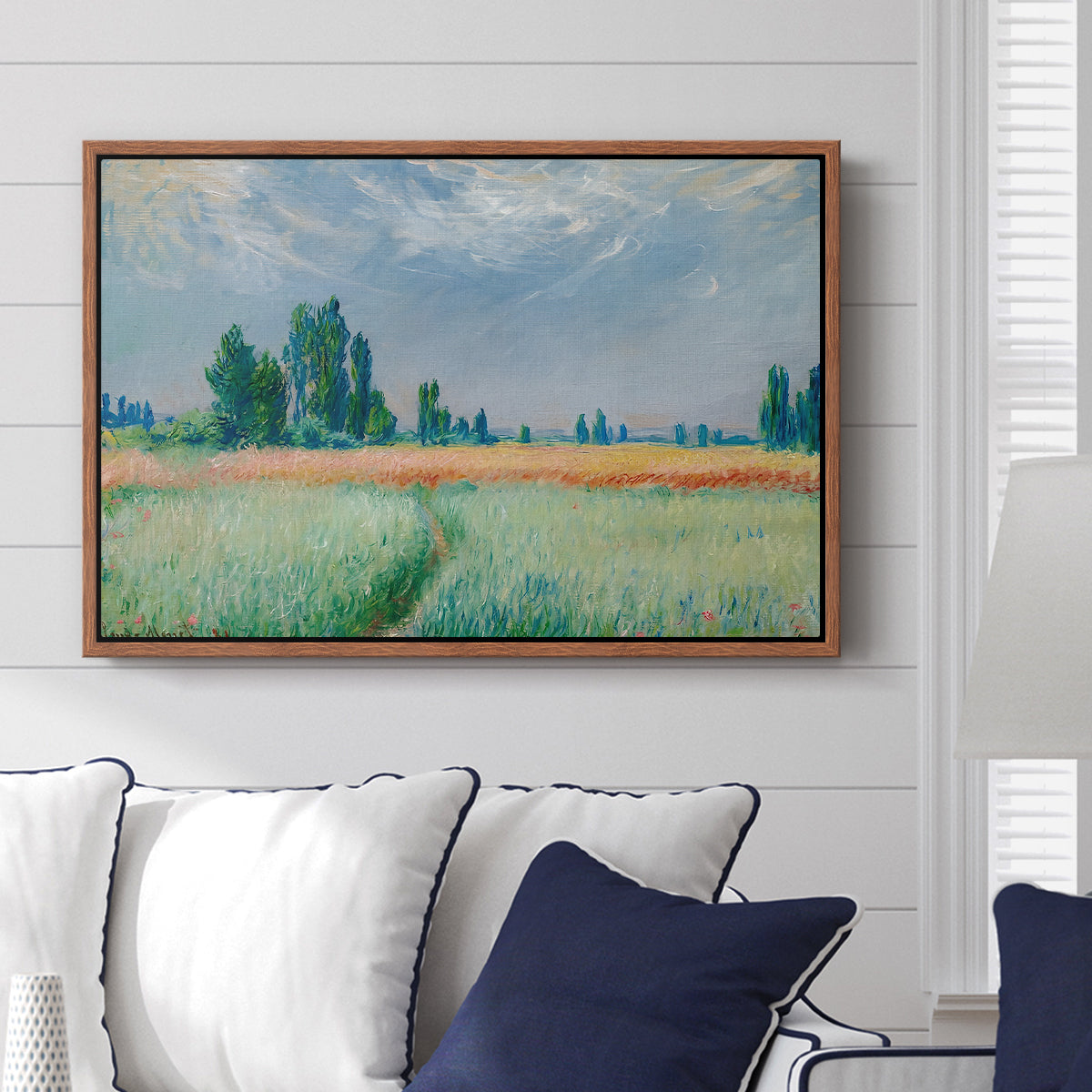The Wheat Field (Champ de Blé), 1881 by Claude Monet displayed above a sofa in a living room in a walnut floater frame, featuring an impressionist depiction of ripened grain field in countryside.