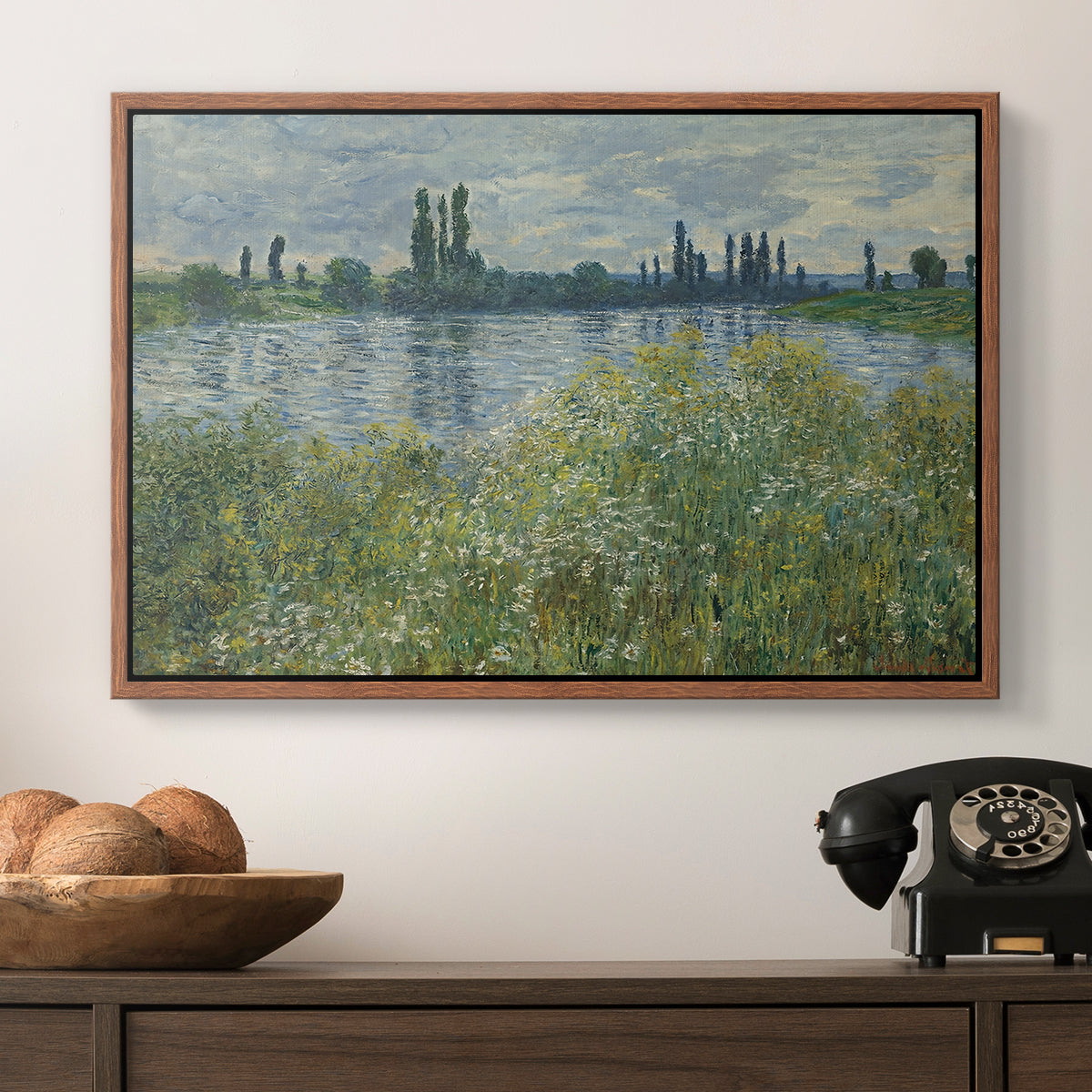 Banks of the Seine, Vétheuil, 1880 by Claude Monet in a walnut floater framed canvas displayed above a console table in a hallway, featuring a natural landscape with calm water and soft foliage.
