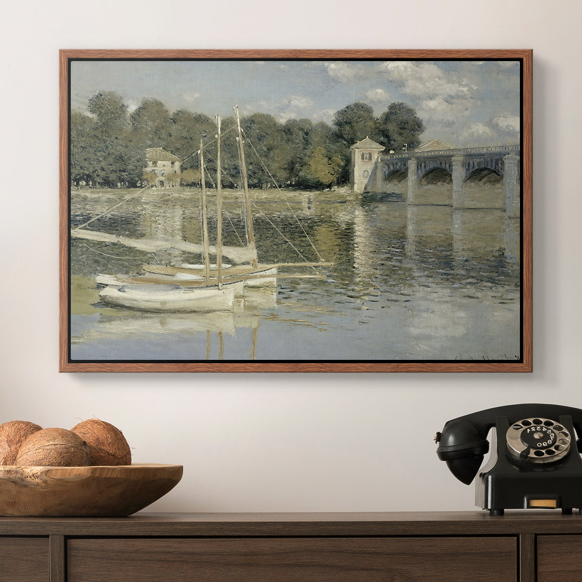 The Bridge at Argenteuil, 1874 by Claude Monet in a walnut floater framed canvas displayed above a console table in a hallway, featuring a riverside view with architecture and nautical activity.