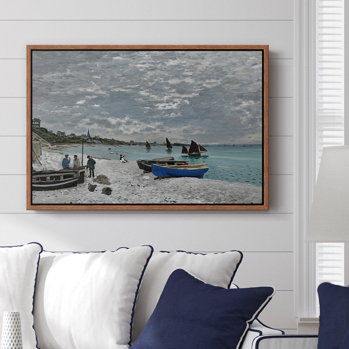 The Beach at Sainte-Adresse, 1867 by Claude Monet displayed above a sofa in a living room in a walnut floater frame, featuring a lively beach scene with people overlooking water and ships.