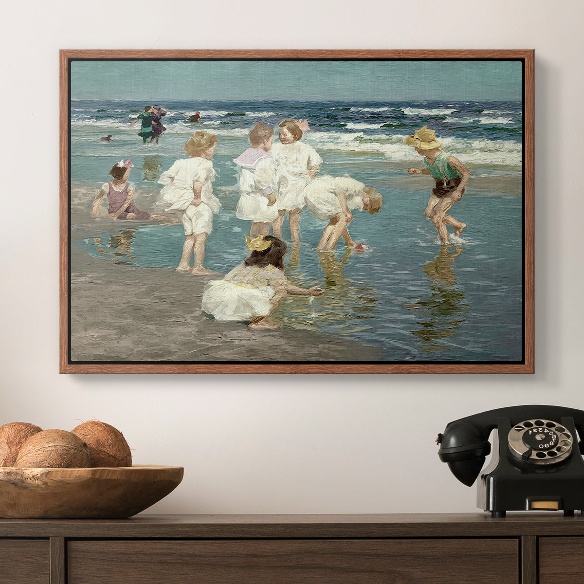 A Holiday, c. 1915 by Edward Henry Potthast in a walnut floater framed canvas displayed above a console table in a hallway, featuring a lively shoreline scene with people gathered in surf.
