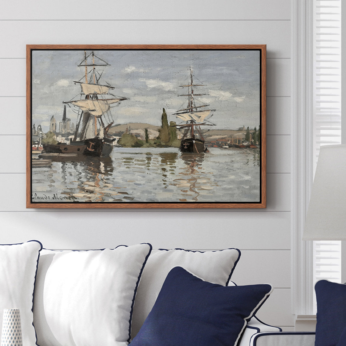 Ships Riding on the Seine at Rouen, 1872 by Claude Monet displayed above a sofa in a living room in a walnut floater frame, featuring an impressionist river scene with anchored sailing ships and reflections.