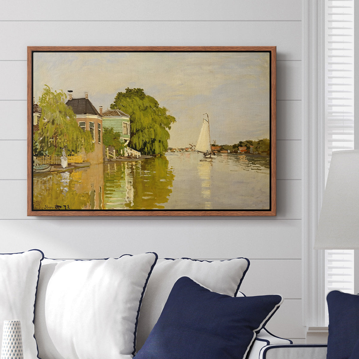 Houses on the Achterzaan, 1871 by Claude Monet displayed above a sofa in a living room in a walnut floater frame, featuring riverside homes with trees and mirrored reflections in water.