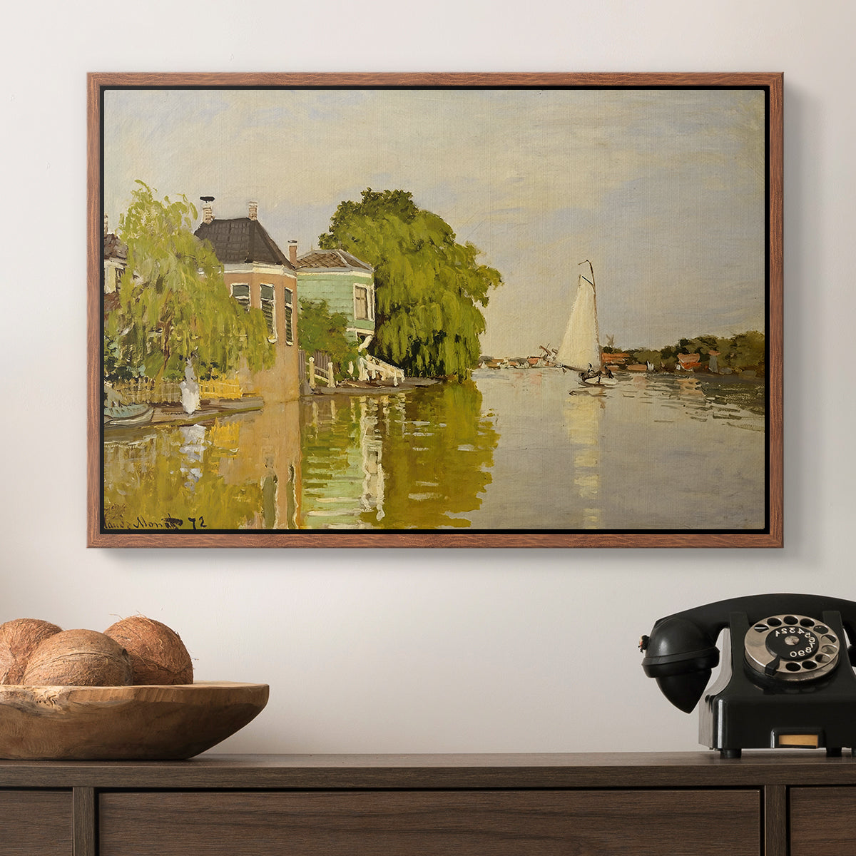 Houses on the Achterzaan, 1871 by Claude Monet in a walnut floater framed canvas displayed above a console table in a hallway, featuring a peaceful village scene with houses bordering water.