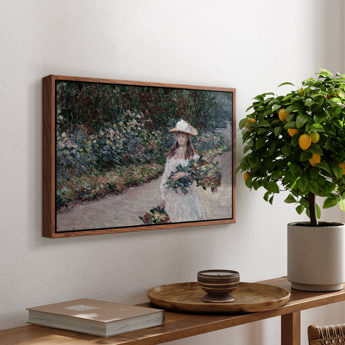 Young Girl in the Garden at Giverny, 1888 by Claude Monet, presented in a walnut floater framed canvas featuring a young girl seated in lush garden surrounded by blooming flowers, displayed above a hallway console table.