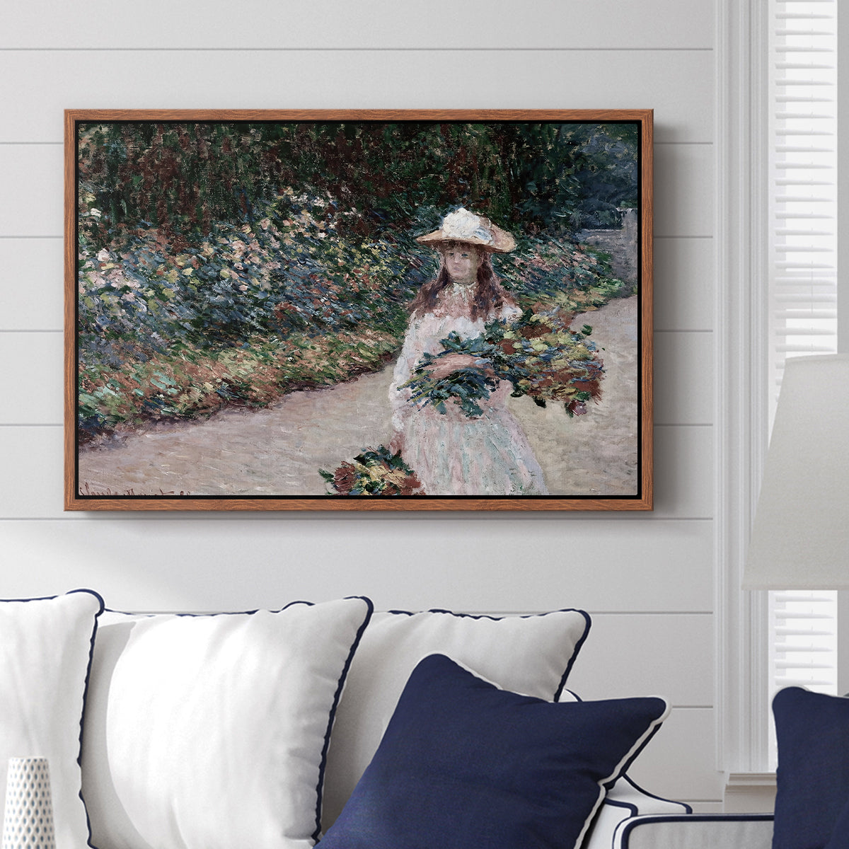 Young Girl in the Garden at Giverny, 1888 by Claude Monet displayed above a sofa in a living room in a walnut floater frame, featuring an impressionist garden scene with child among greenery and blossoms.