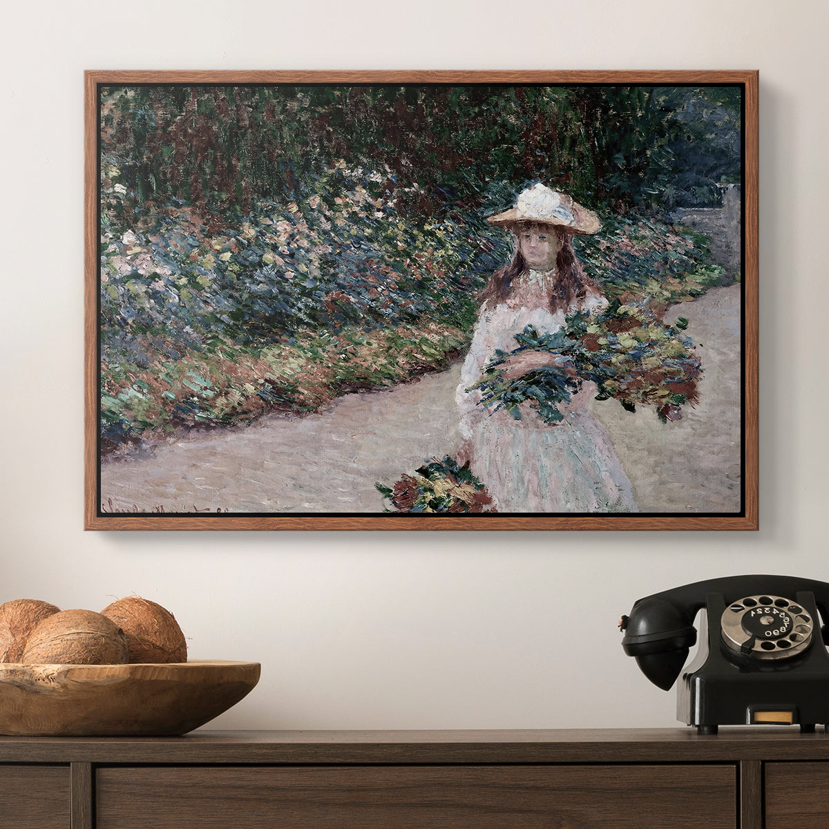 Young Girl in the Garden at Giverny, 1888 by Claude Monet in a walnut floater framed canvas displayed above a console table in a hallway, featuring a tranquil outdoor portrait of girl in floral setting.