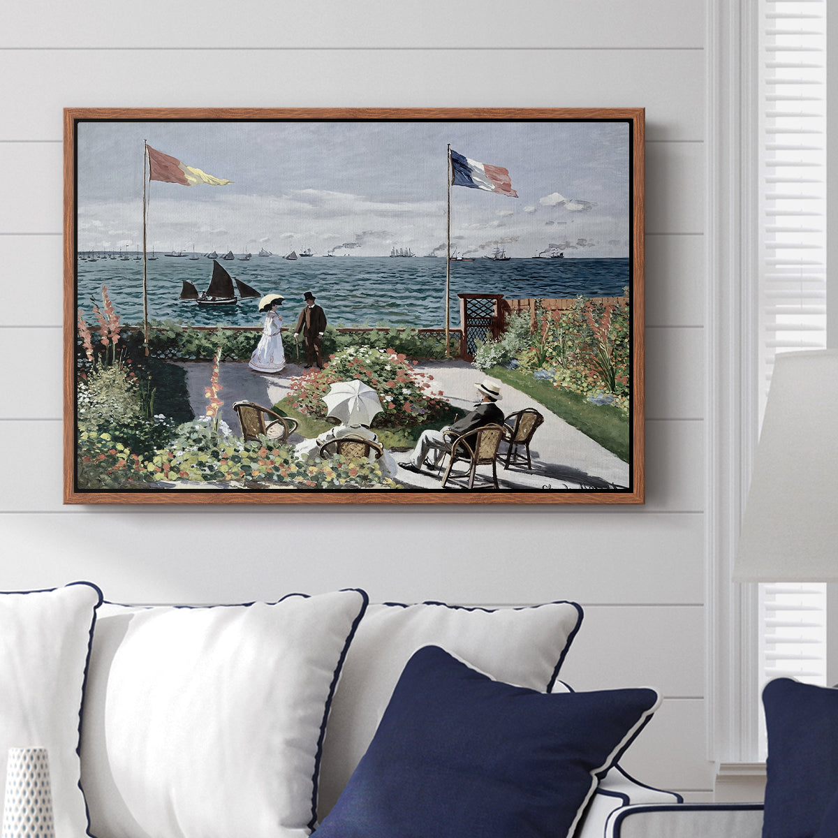 Garden at Sainte-Adresse, 1867 by Claude Monet displayed above a sofa in a living room in a walnut floater frame, featuring an impressionist coastal garden with people and ocean view.