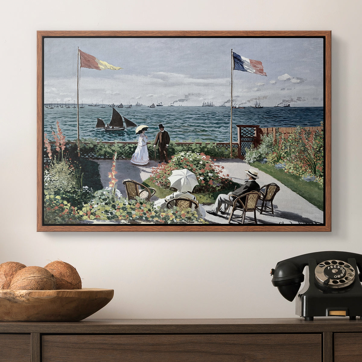 Garden at Sainte-Adresse, 1867 by Claude Monet in a walnut floater framed canvas displayed above a console table in a hallway, featuring a landscaped terrace with figures and flags near shoreline.