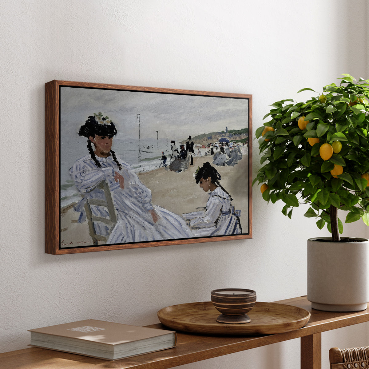 On the Beach at Trouville, 1870 by Claude Monet, presented in a walnut floater framed canvas featuring figures seated on beach with parasols facing the ocean, displayed above a hallway console table.
