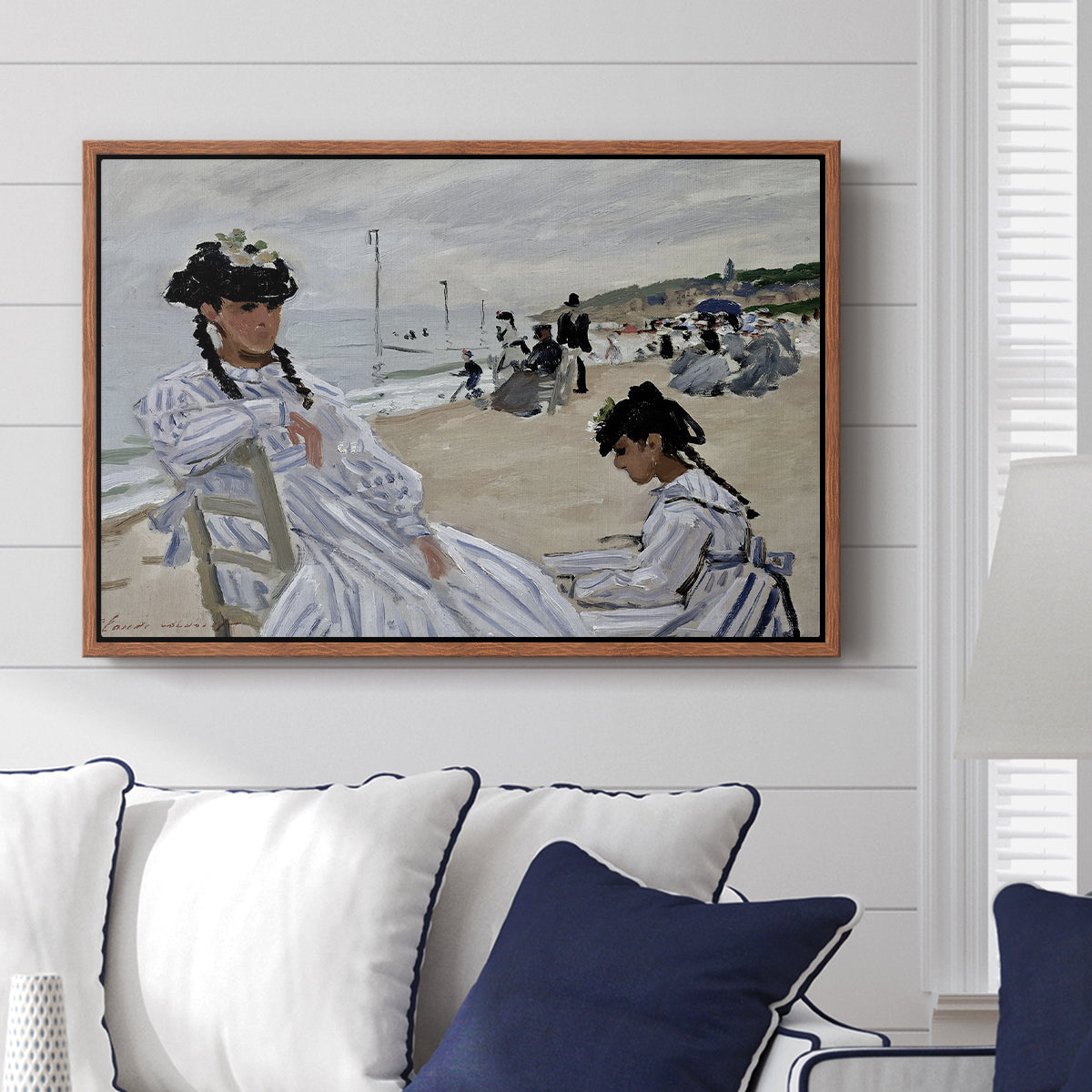 On the Beach at Trouville, 1870 by Claude Monet displayed above a sofa in a living room in a walnut floater frame, featuring an impressionist seaside scene with women in dresses and hats.