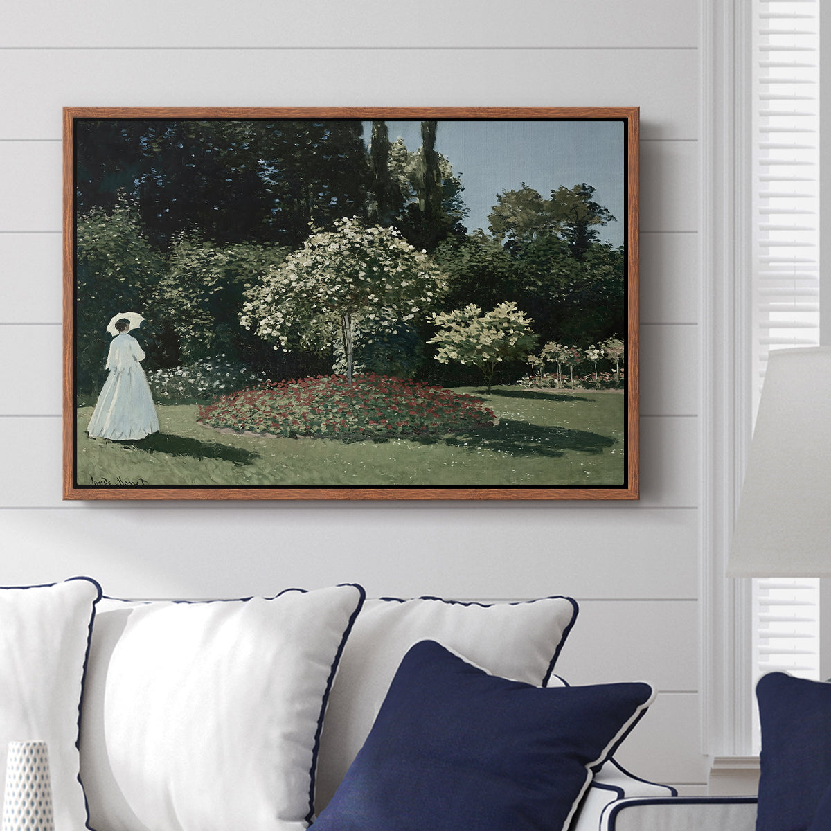 Woman in the Garden, Sainte-Adresse, 1867 by Claude Monet displayed above a sofa in a living room in a walnut floater frame, featuring an impressionist figure in sunlit garden with lush vegetation.