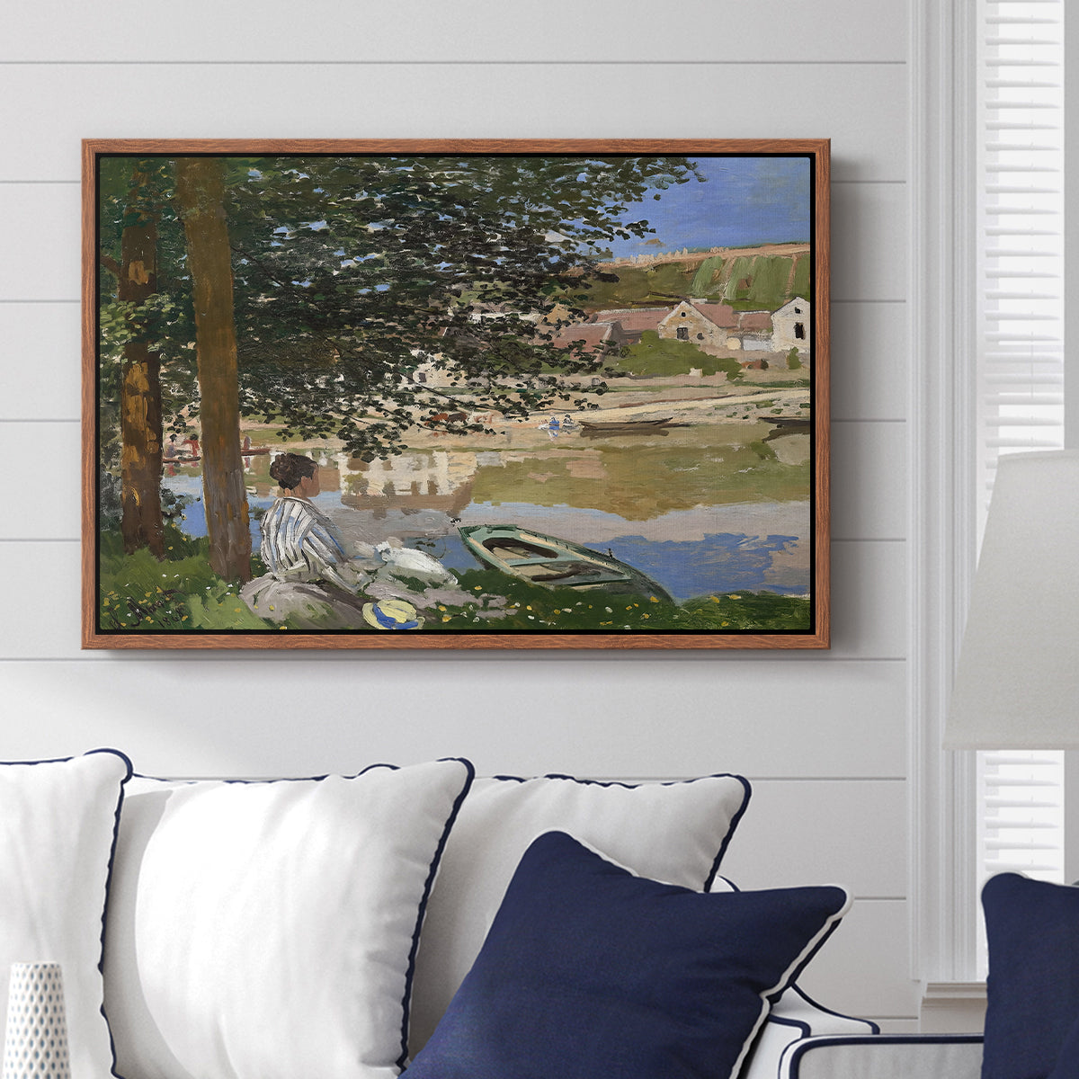 On the Bank of the Seine, Bennecourt, 1868 by Claude Monet displayed above a sofa in a living room in a walnut floater frame, featuring a peaceful riverside scene with figures resting in grassy area by water.