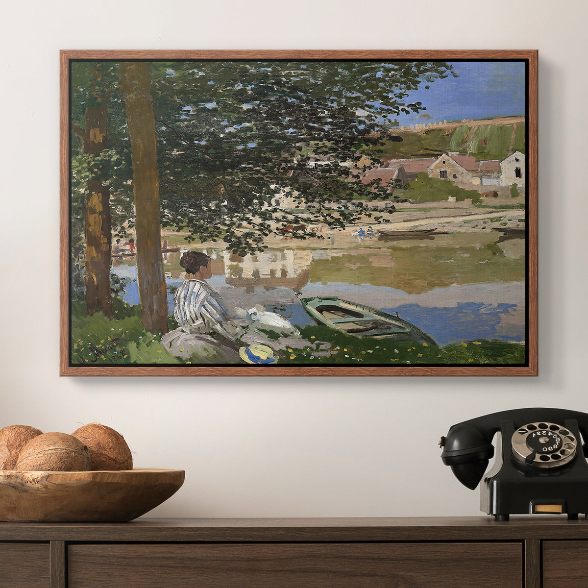 On the Bank of the Seine, Bennecourt, 1868 by Claude Monet in a walnut floater framed canvas displayed above a console table in a hallway, featuring a quiet outdoor setting with figures near river under foliage.