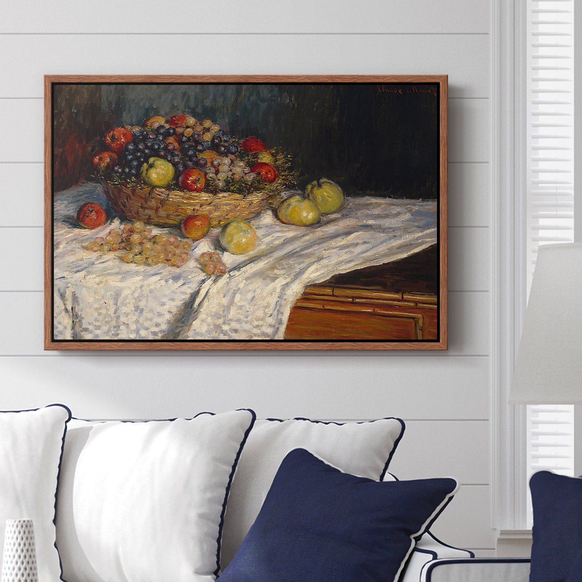 Still Life with Apples and Grapes, 1880 by Claude Monet displayed above a sofa in a living room in a walnut floater frame, featuring an impressionist still life of fruit placed on cloth-covered surface.