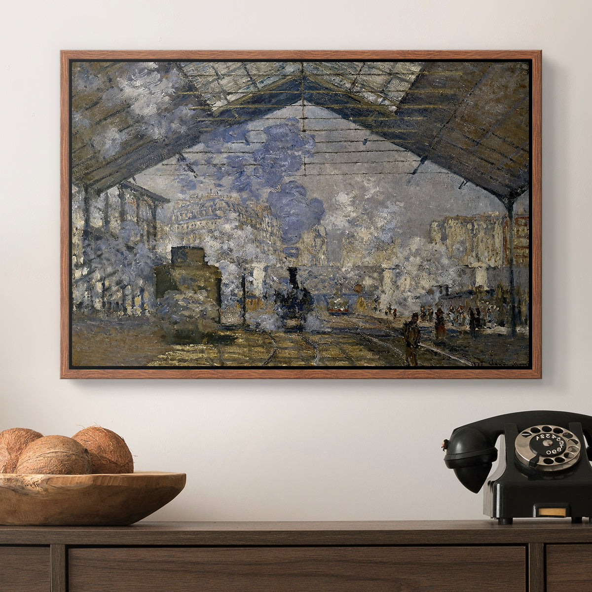 The Gare Saint-Lazare, 1877 by Claude Monet in a walnut floater framed canvas displayed above a console table in a hallway, featuring a bustling transport hub with trains beneath glass roof.