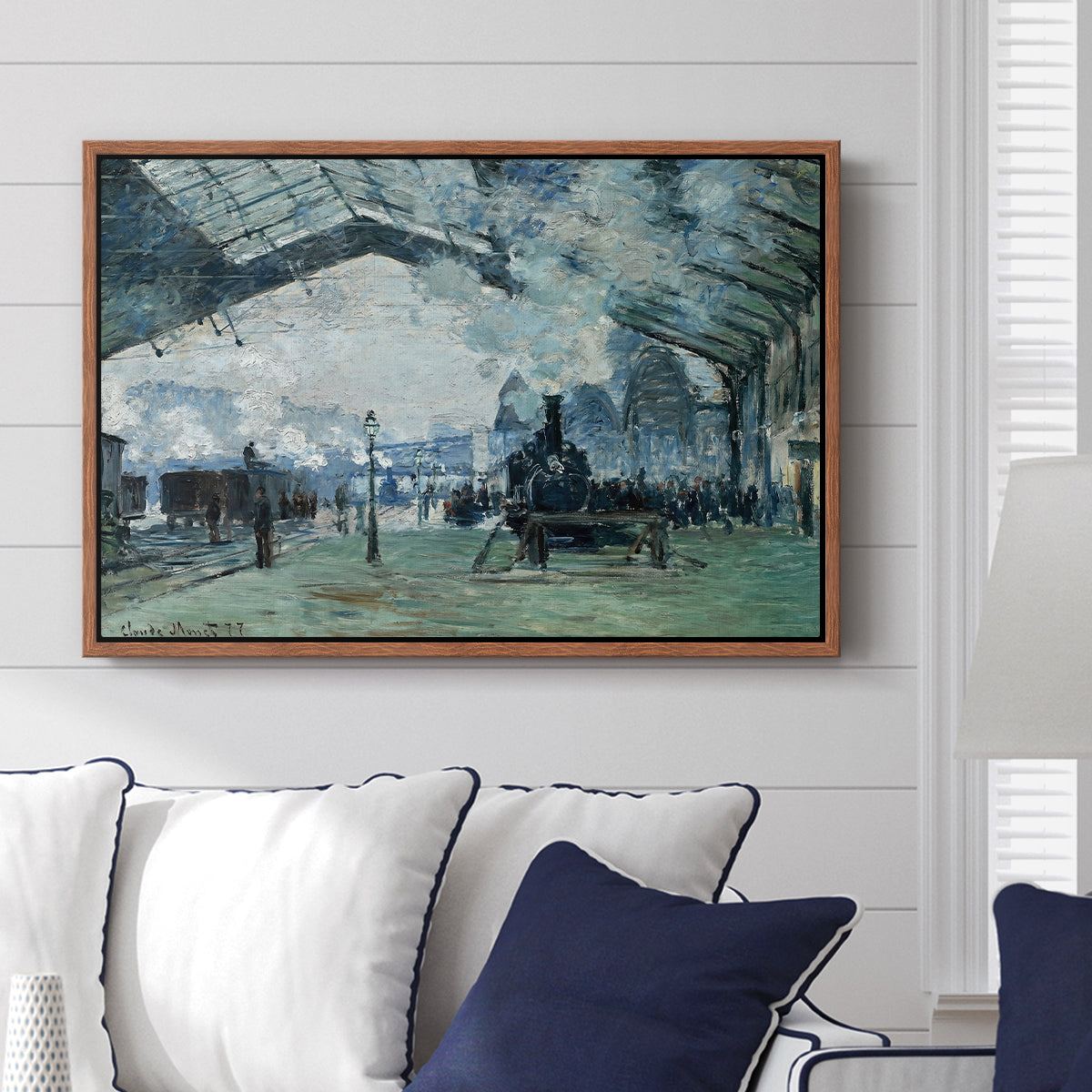 The Saint-Lazare Station, 1877 by Claude Monet displayed above a sofa in a living room in a walnut floater frame, featuring an impressionist railway scene with locomotives and haze.