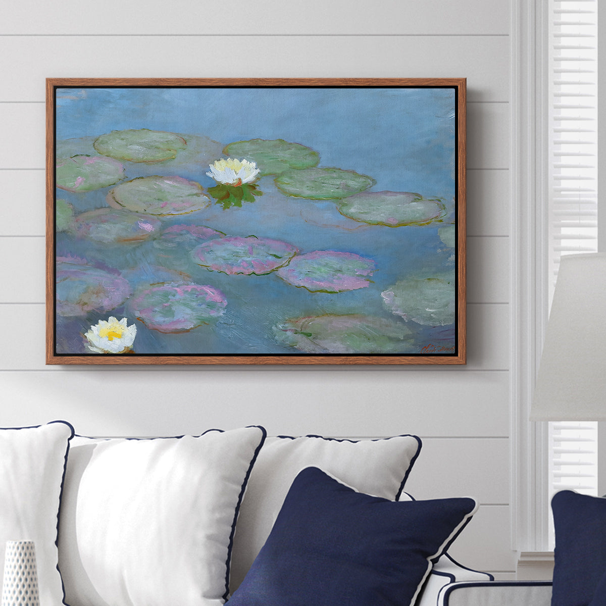 Water Lilies (Nymphéas), 1897-1899 by Claude Monet displayed above a sofa in a living room in a walnut floater frame, featuring an impressionist pond scene with lily pads and soft reflections.