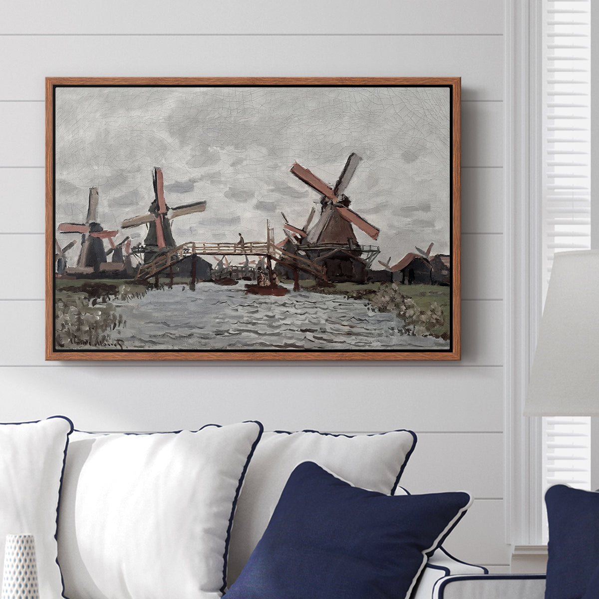 Windmills near Zaandam, 1871 by Claude Monet displayed above a sofa in a living room in a walnut floater frame, featuring an impressionist view of Dutch windmills along riverbank.