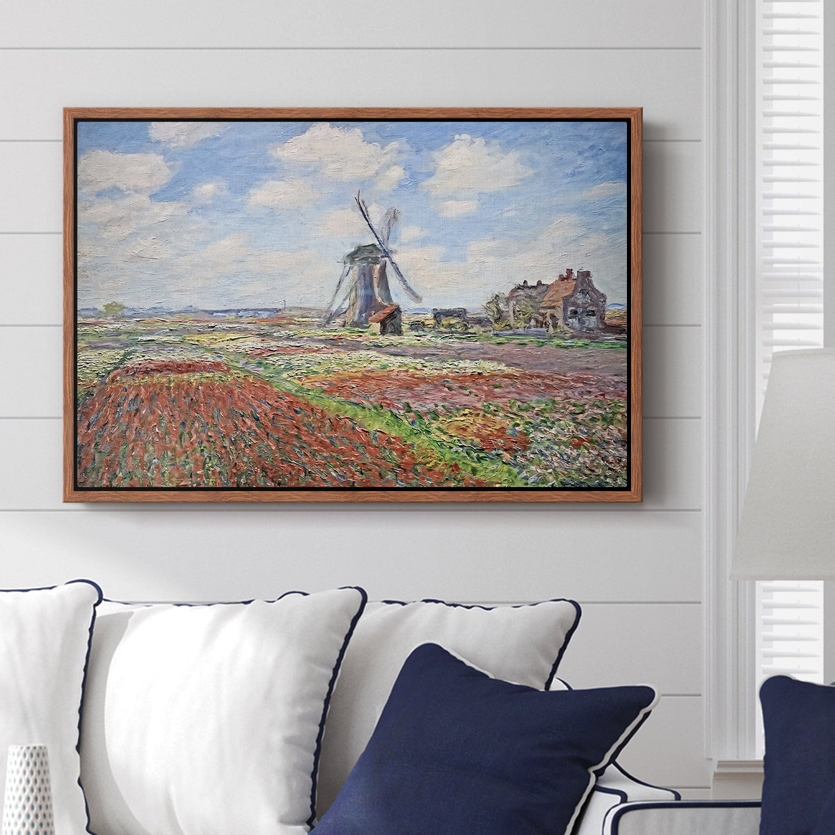 Tulip Fields with the Rijnsburg Windmill, 1886 by Claude Monet displayed above a sofa in a living room in a walnut floater frame, featuring a vibrant agricultural landscape with flowers and windmill.