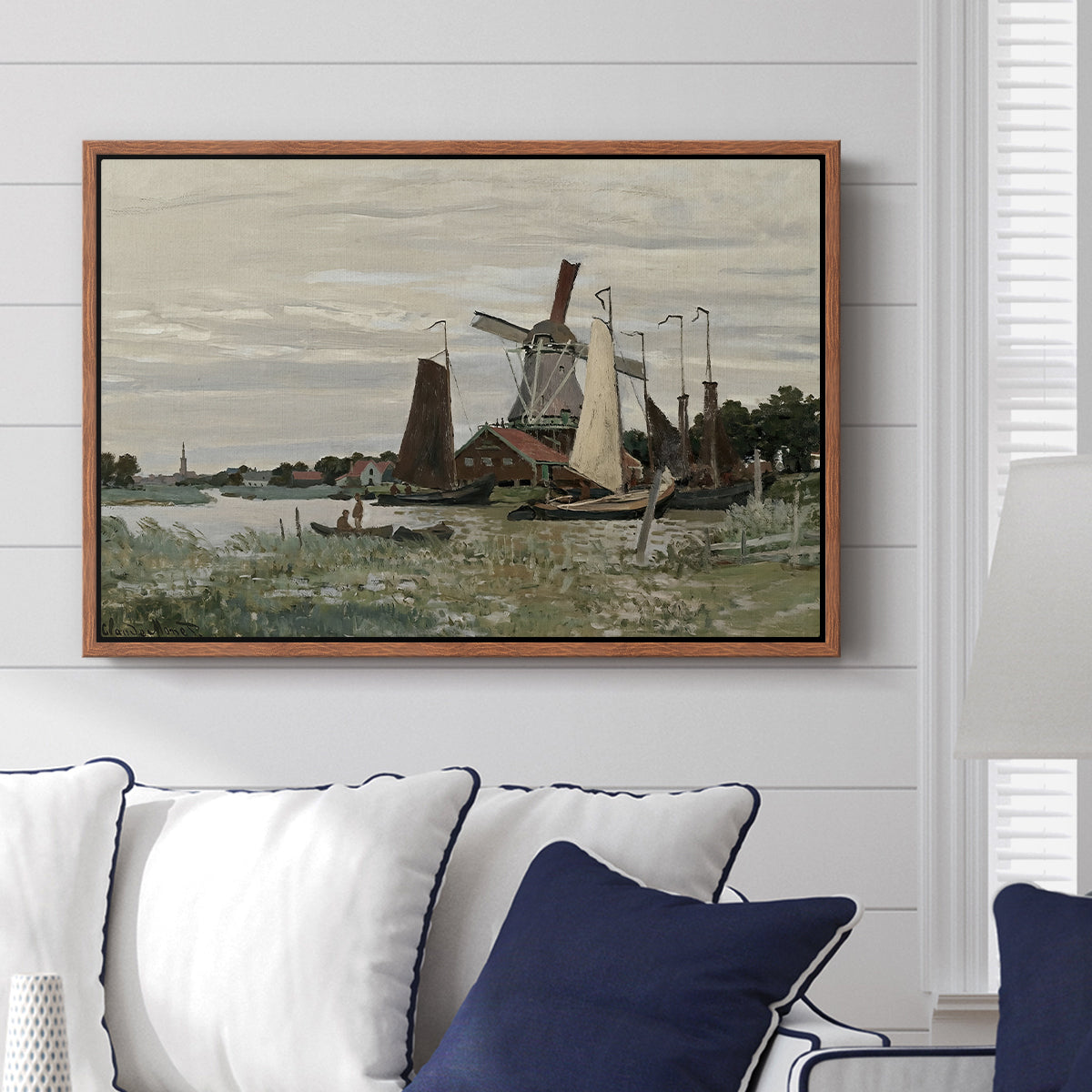 Windmill at Zaandam, 1871 by Claude Monet displayed above a sofa in a living room in a walnut floater frame, featuring an impressionist depiction of windmill near riverbank.