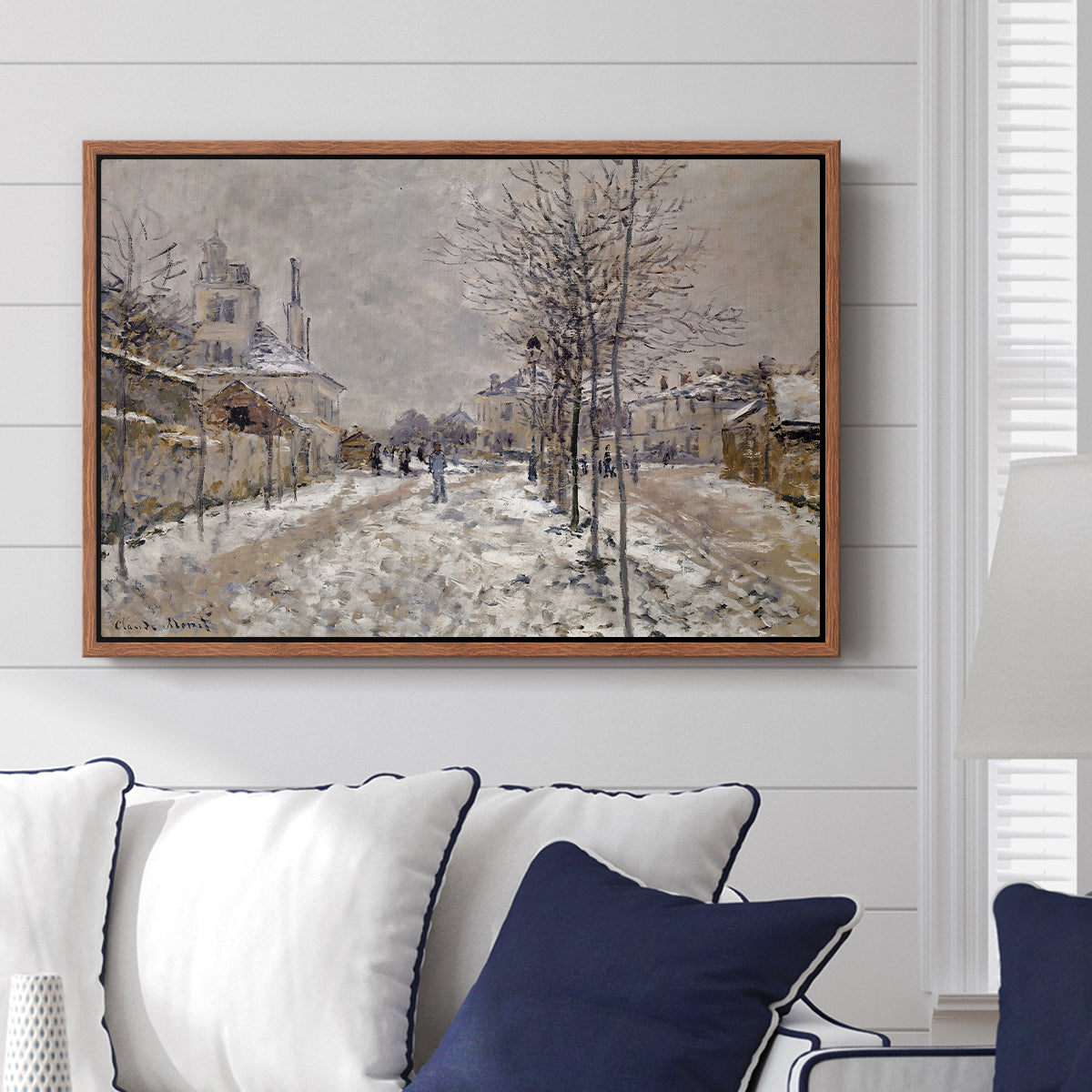 The Boulevard de Pontoise at Argenteuil, Snow Effect, 1875 by Claude Monet displayed above a sofa in a living room in a walnut floater frame, featuring an impressionist winter scene with road and bare trees.
