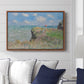 The Cliff Walk at Pourville, 1882 by Claude Monet displayed above a sofa in a living room in a walnut floater frame, featuring an impressionist seaside landscape with people strolling above water.