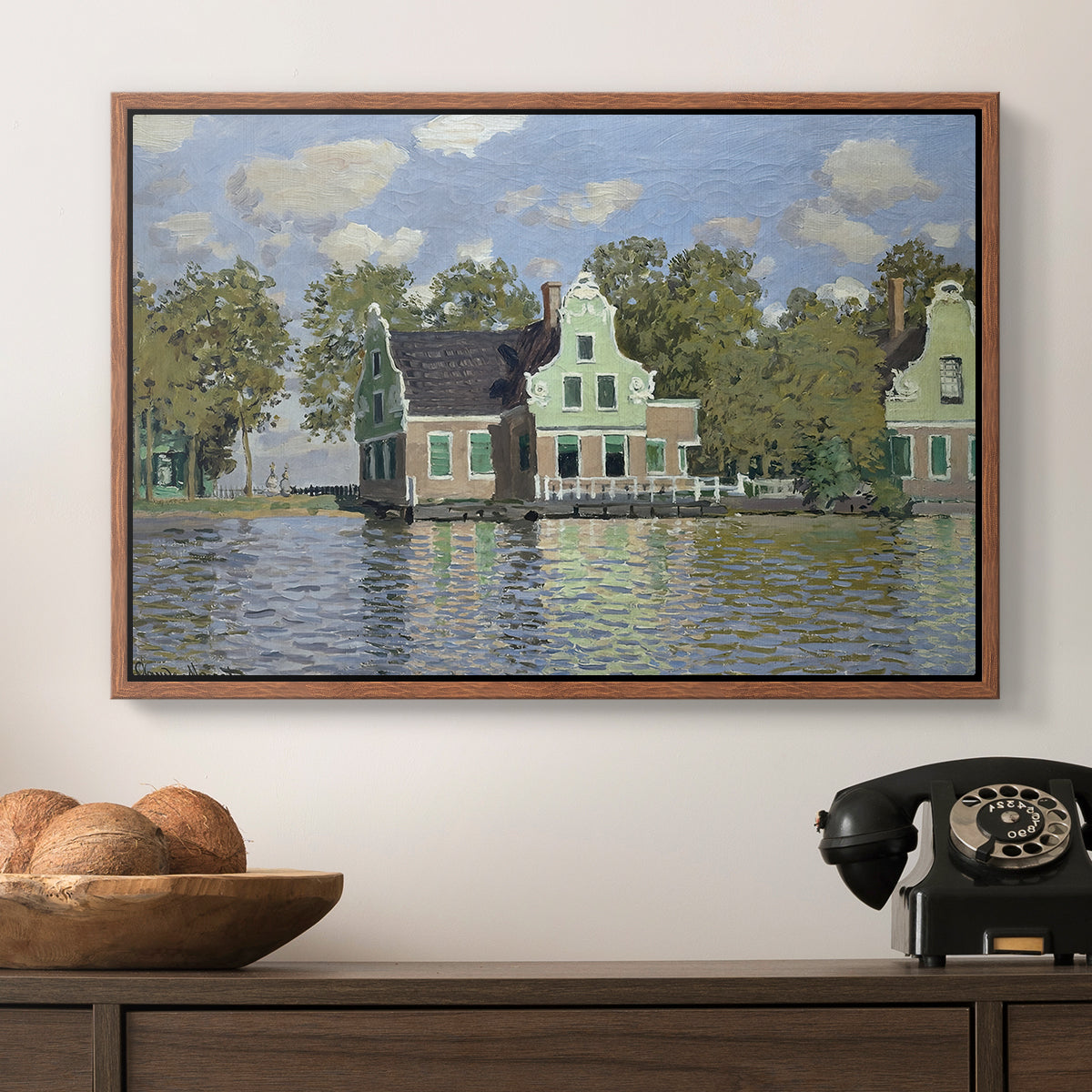 Houses on the Zaan River at Zaandam, 1871 by Claude Monet in a walnut floater framed canvas displayed above a console table in a hallway, featuring a waterfront architecture with still reflections.