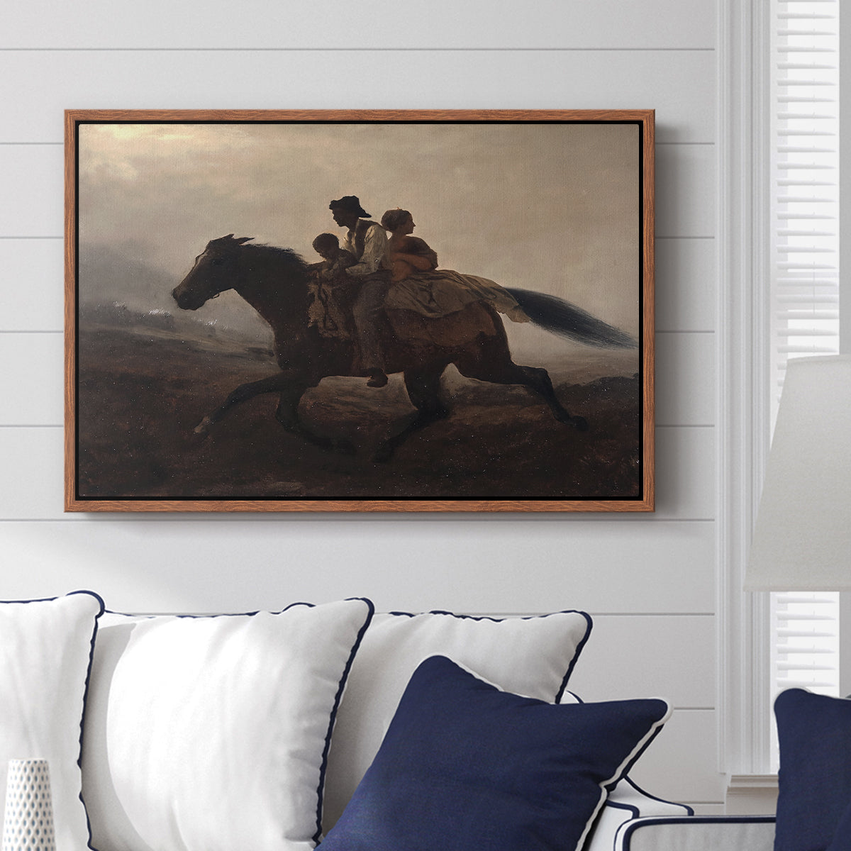A Ride for Liberty – The Fugitive Slaves, c. 1862 by Eastman Johnson displayed above a sofa in a living room in a walnut floater frame, featuring a dramatic scene of enslaved people fleeing on horseback in darkness.