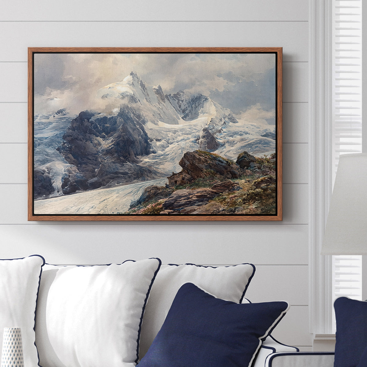 The Grossglockner, 1880 by Edward Theodore Compton displayed above a sofa in a living room in a walnut floater frame, featuring a dramatic mountain summit with snow and rugged slopes.