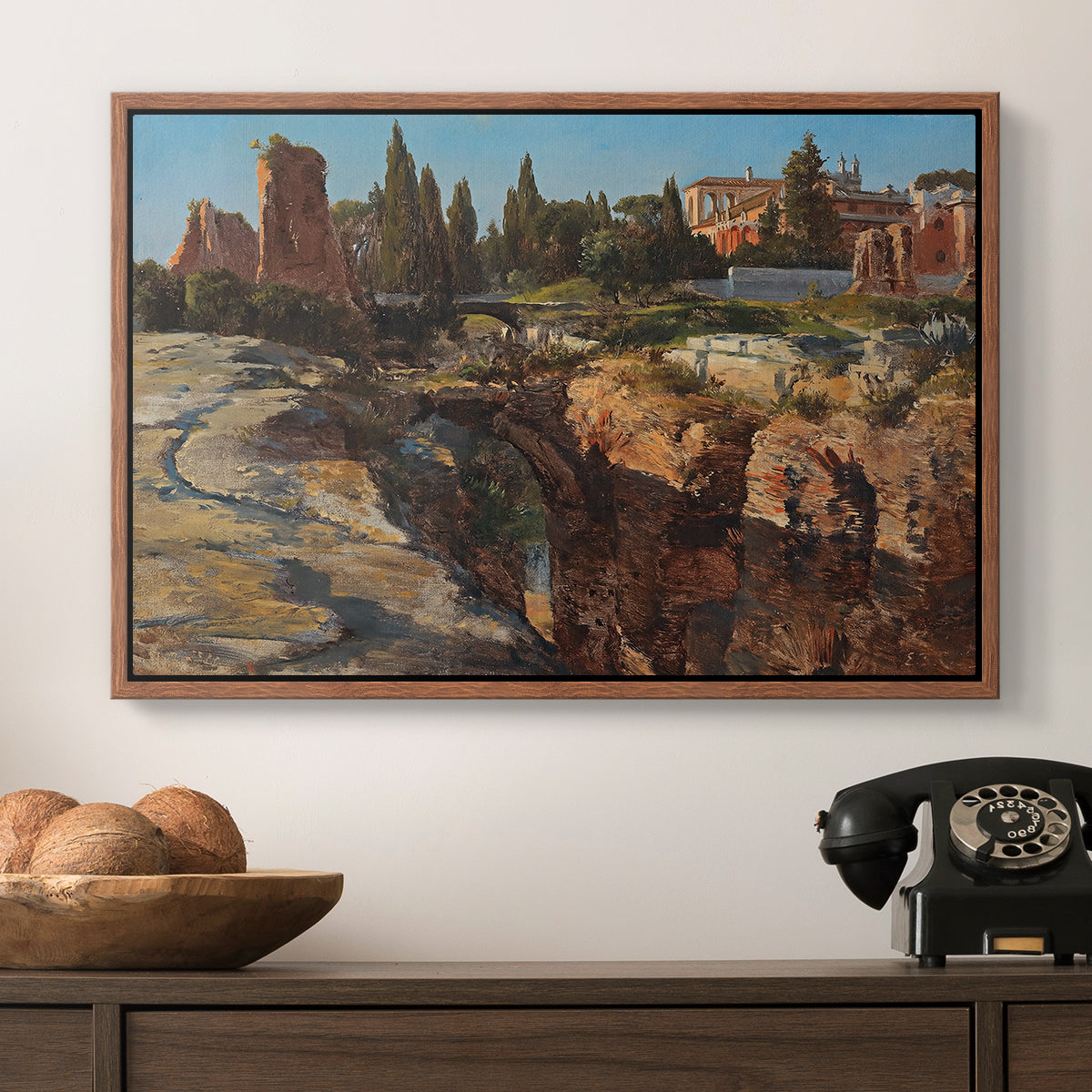 Palatine in Rome, c. 1921 by Edward Theodore Compton in a walnut floater framed canvas displayed above a console table in a hallway, featuring a detailed depiction of historic Roman architecture.