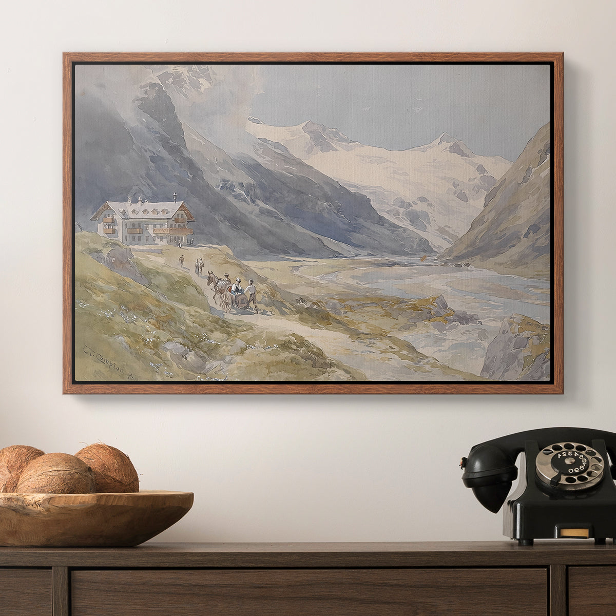 Shepherds (Pasterze), c. 1921 by Edward Theodore Compton in a walnut floater framed canvas displayed above a console table in a hallway, featuring a natural landscape with human presence among mountains.