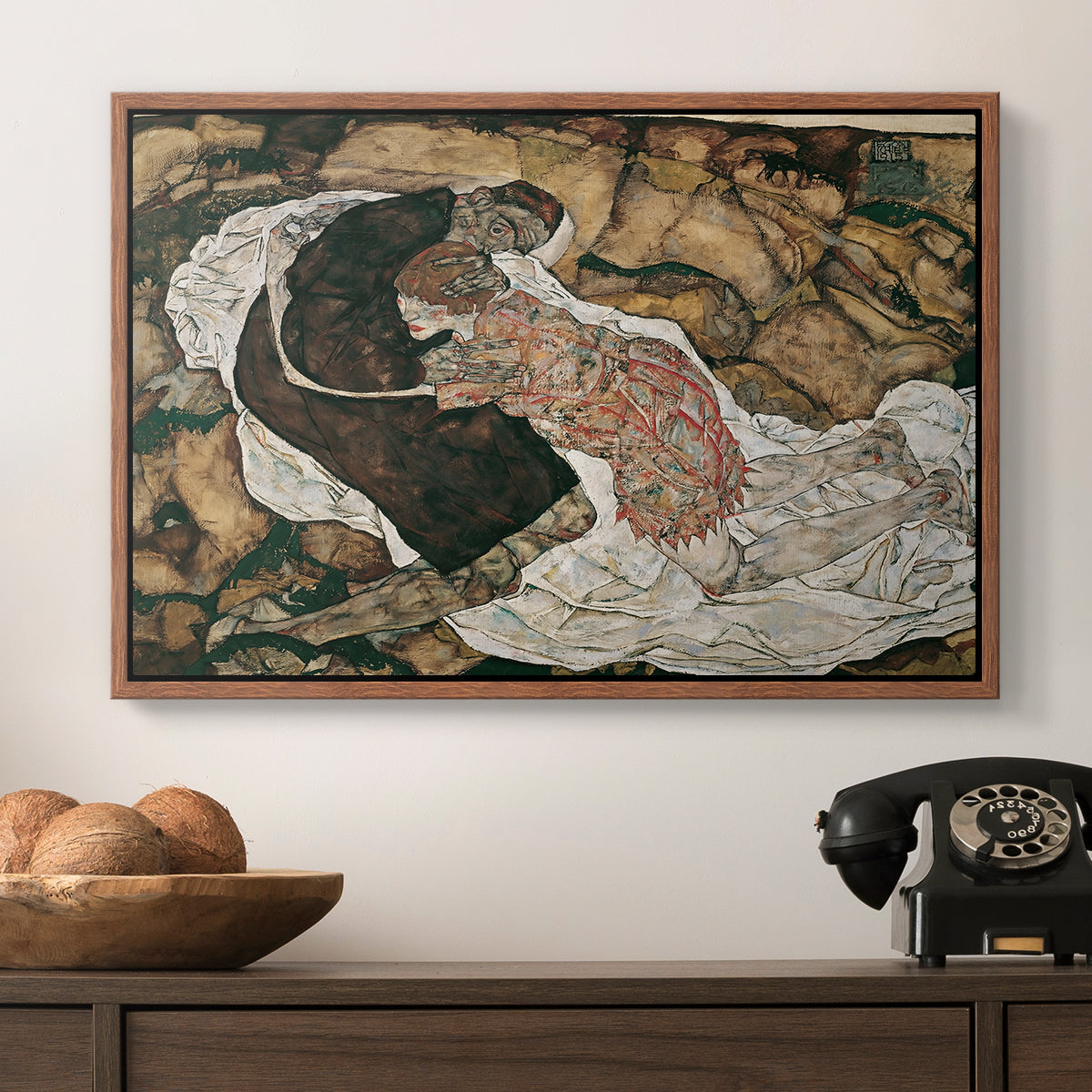 Death and the Maiden, 1915 by Egon Schiele in a walnut floater framed canvas displayed above a console table in a hallway, featuring an intense composition exploring life and death through figures.