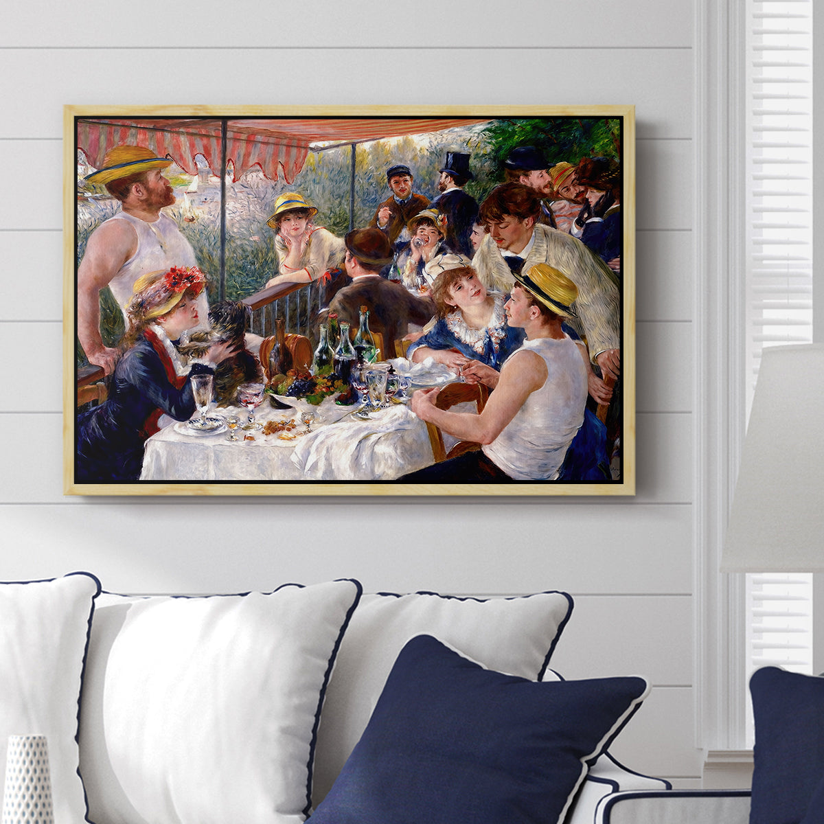 Luncheon of the Boating Party (Le Déjeuner des canotiers), 1880-1881 by Pierre-Auguste Renoir displayed above a sofa in a living room in a natural wood floater frame, featuring a lively gathering of men and women eating and socializing at outdoor table.