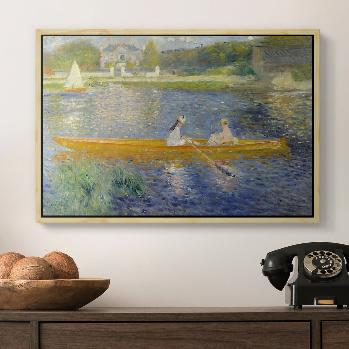 The Skiff (La Yole), 1875 by Pierre-Auguste Renoir in a natural wood floater framed canvas displayed above a console table in a hallway, featuring a leisure scene of figures in a small rowboat on tranquil water.
