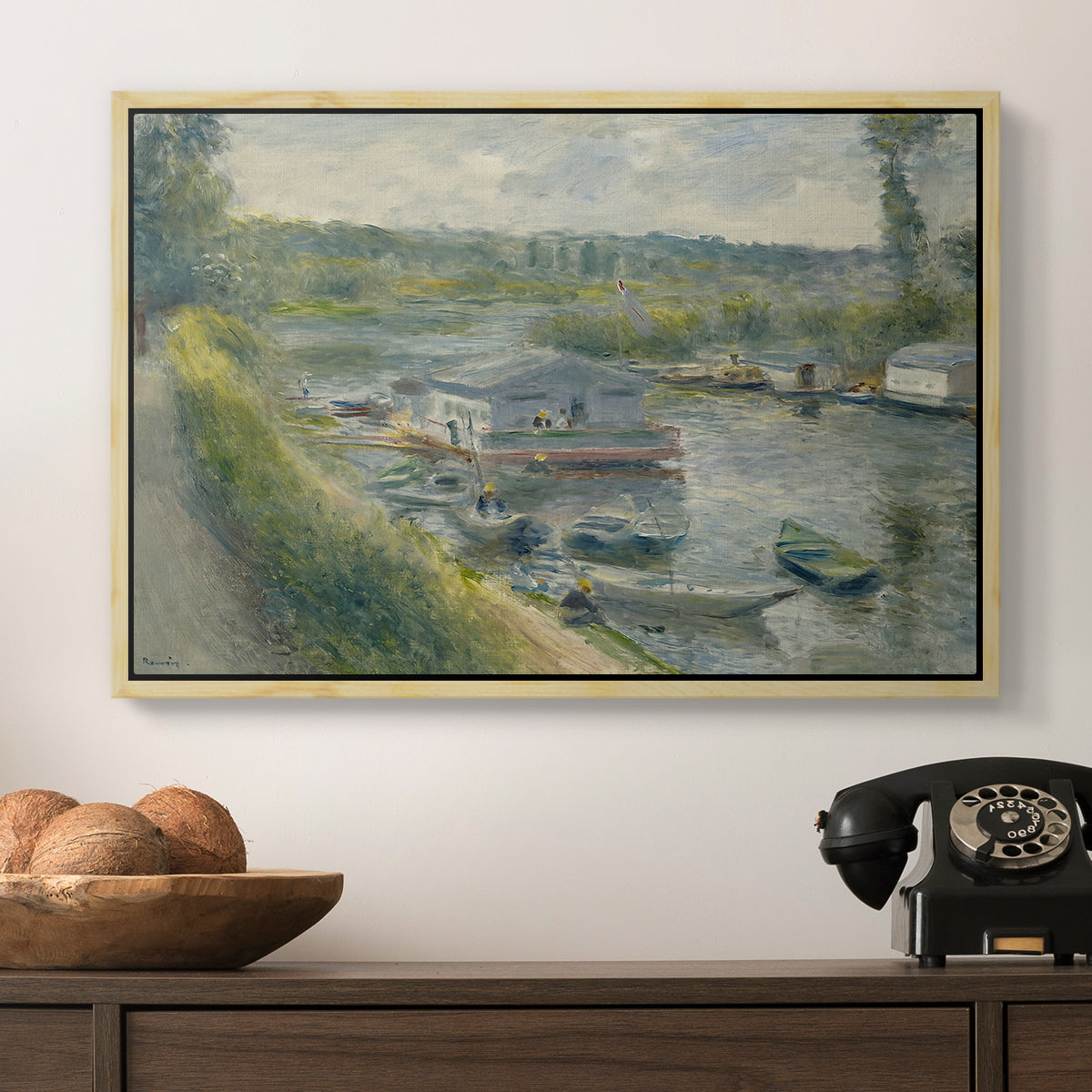 Wash-House Boat at Bas-Meudon, c. 1874 by Pierre-Auguste Renoir in a natural wood floater framed canvas displayed above a console table in a hallway, featuring an everyday life scene with boat and figures along river edge.