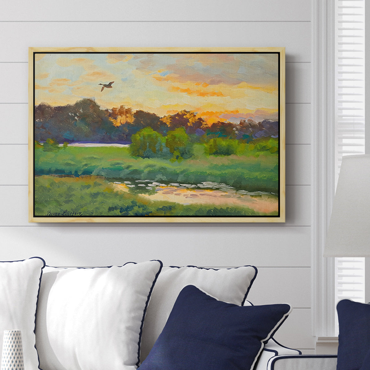 Flying Duck at Sunset, 1924 by Bruno Liljefors displayed above a sofa in a living room in a natural wood floater frame, featuring a lone duck soaring over a glowing marshland.