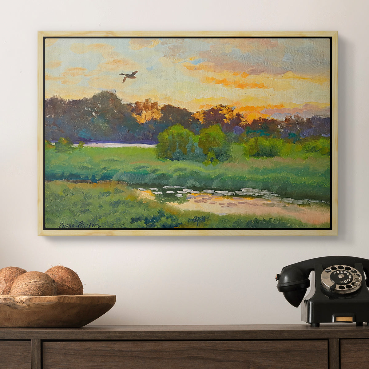Flying Duck at Sunset, 1924 by Bruno Liljefors in a natural wood floater framed canvas displayed above a console table in a hallway, featuring a lone duck flying over a marsh at golden hour.