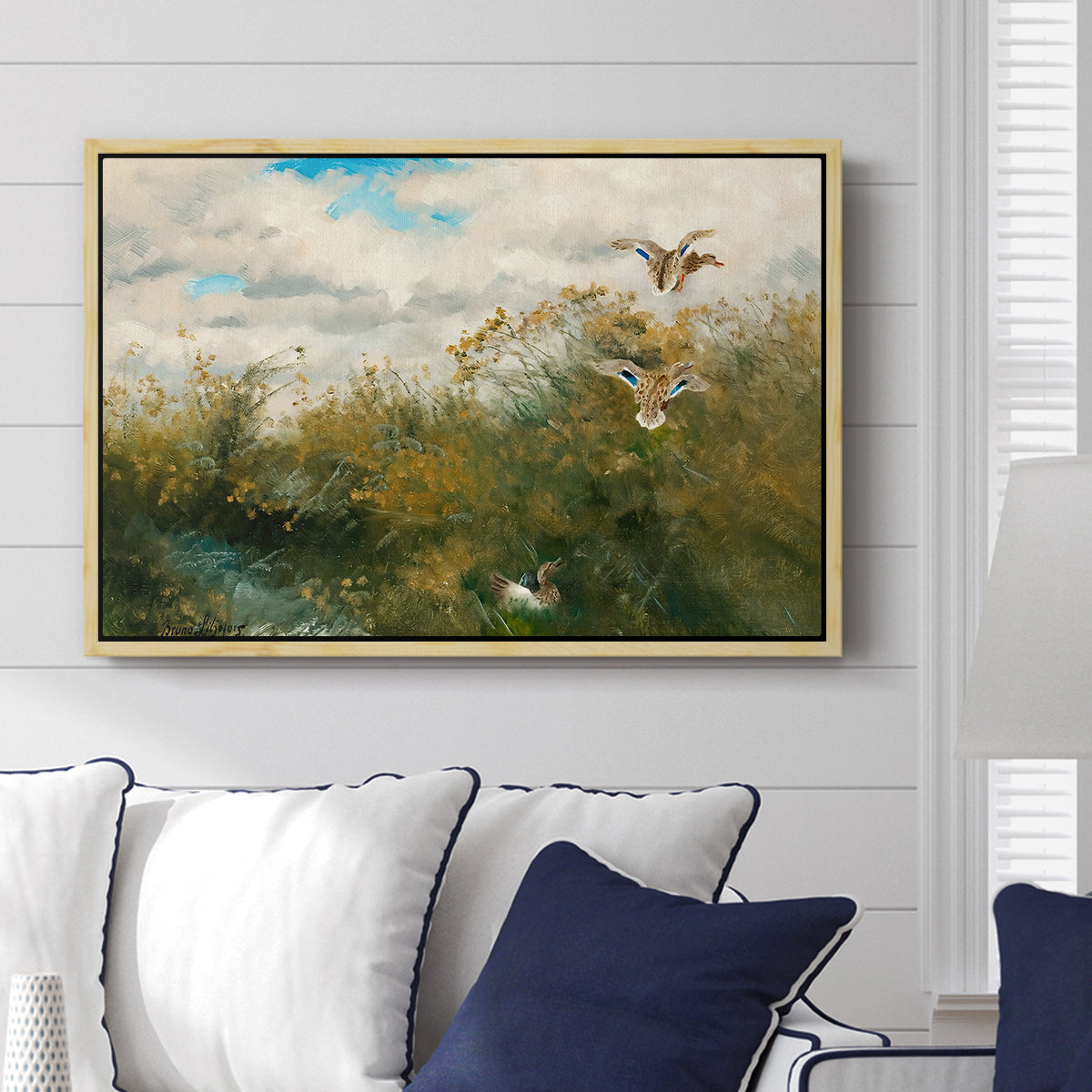 Wild Ducks (Grasänder), 1890 by Bruno Liljefors displayed above a sofa in a living room in a natural wood floater frame, featuring a wildlife scene of ducks walking through tall grass beside water.