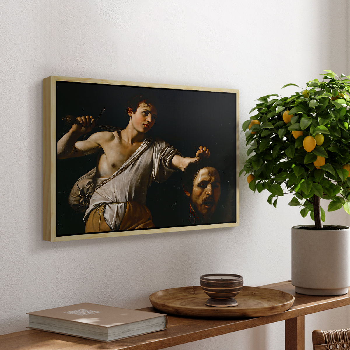 David with the Head of Goliath (Vienna Version), c. 1607 by Caravaggio, presented in a natural wood floater framed canvas featuring a young David holding the severed head of Goliath against a dark background, displayed above a hallway console table.