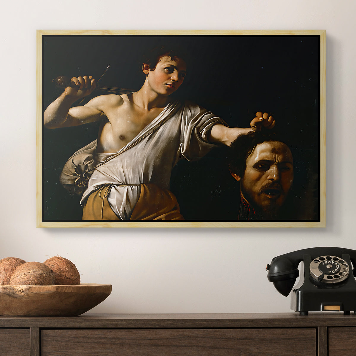 David with the Head of Goliath (Vienna Version), c. 1607 by Caravaggio in a natural wood floater framed canvas displayed above a console table in a hallway, featuring an intense religious scene with figure emerging from darkness holding trophy.