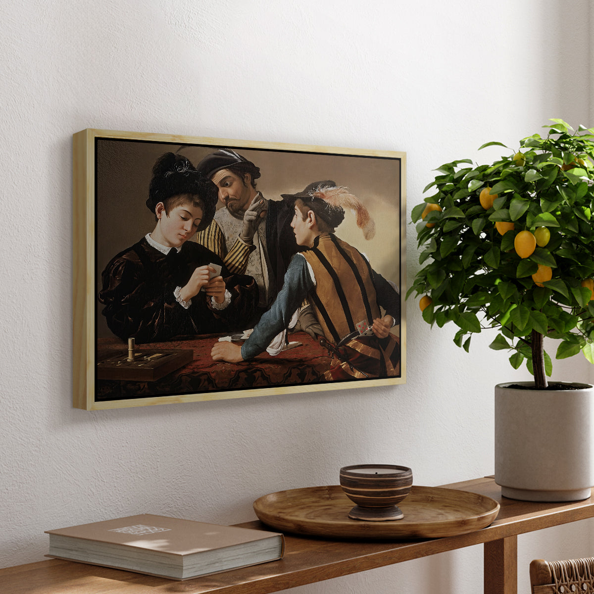 The Cardsharps, c. 1594 by Caravaggio, presented in a natural wood floater framed canvas featuring two men cheating at cards while a third figure secretly observes behind them, displayed above a hallway console table.