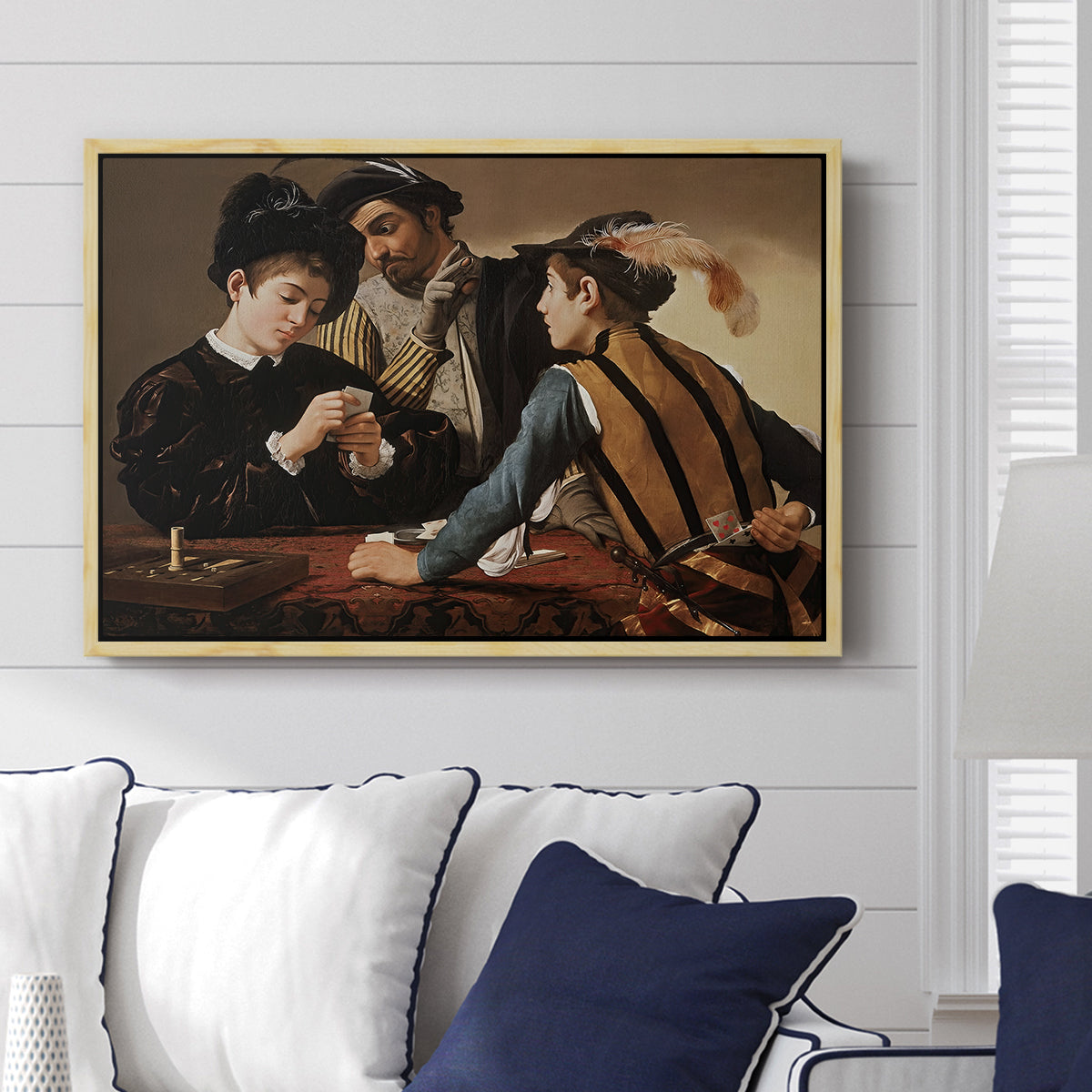 The Cardsharps, c. 1594 by Caravaggio displayed above a sofa in a living room in a natural wood floater frame, featuring a genre scene of card game with deception and hidden accomplice.