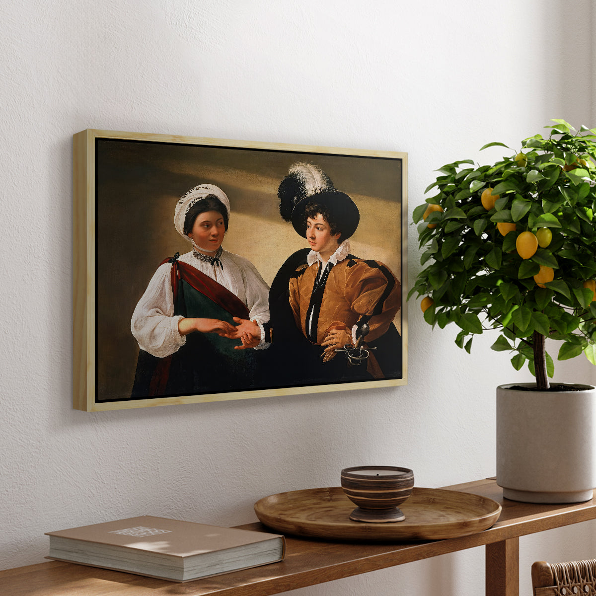 The Fortune Teller (Louvre Version), c. 1595 by Caravaggio, presented in a natural wood floater framed canvas featuring a woman reading a young man's palm while secretly stealing his ring, displayed above a hallway console table.