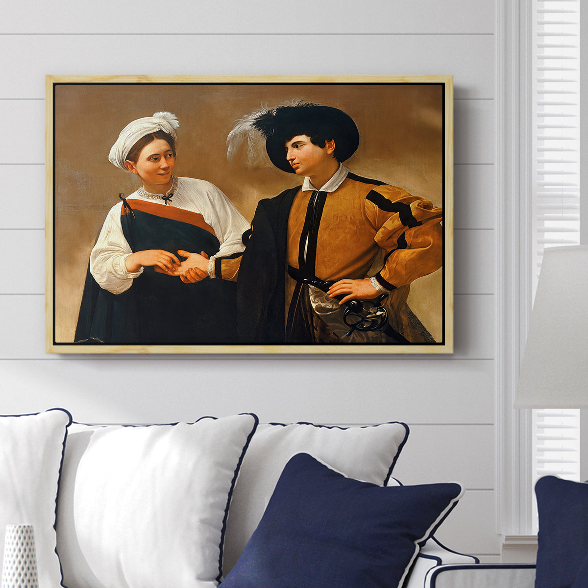 The Fortune Teller (Capitoline Version), c. 1599 by Caravaggio displayed above a sofa in a living room in a natural wood floater frame, featuring a fortune teller tricking young man during palm reading.