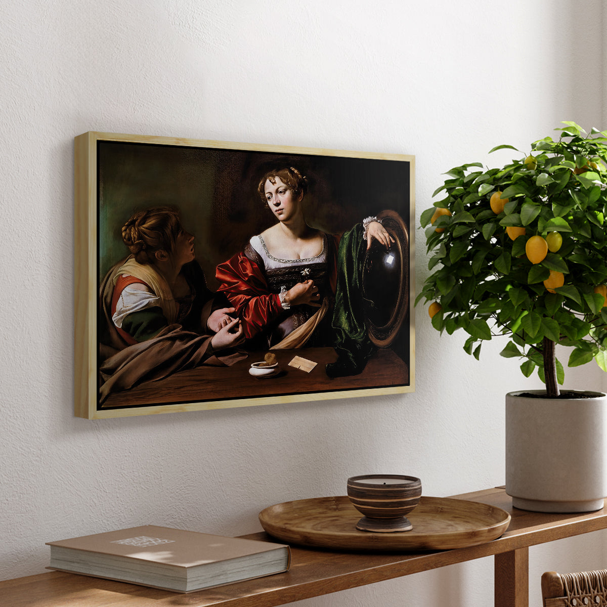Martha and Mary Magdalene, c. 1598 by Caravaggio, presented in a natural wood floater framed canvas featuring a two women seated together in conversation with symbolic objects on table, displayed above a hallway console table.